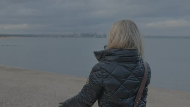 Middle-aged woman takes photo with smartphone while standing on seashore