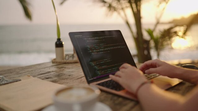 Female developer working on laptop by the ocean. Young woman freelancer coding at outdoor tropical cafe. Caucasian girl working remotely typing on computer at exotic location. Worldwide work concept.