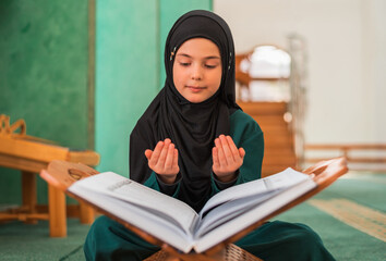 A Muslim prayer girl praying inside the mosque while reading a Quran. 