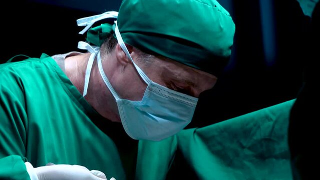 4K, Close-up doctor's face hand doctor doing breast surgery man lying on operating bed, doctor had serious expression on surgery, nurse soaks up blood from surgery cuts knife closely into skin.
