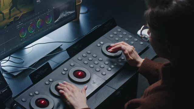 Female editor uses digital color grading control panel. Colorist makes video or photo color correction on computer in studio. Footage and program interface with RGB color wheels and levels on monitor.