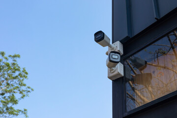 Two white surveillance cameras on black pillars in the garden near buildings on blue background. outdoor security cctv camera
