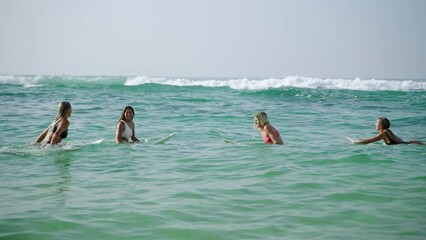 Young diverse women surfers floating on surfboards and riding waves in the ocean at sunrise. Surfer females sitting on surfing boards in calm sea looking at horizon. Girls enjoy water sport lifestyle - Powered by Adobe