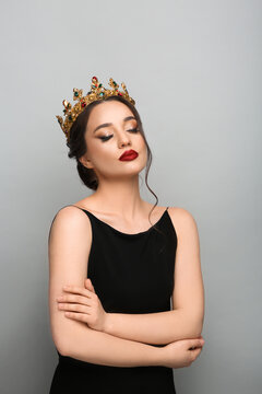 Beautiful young woman wearing luxurious crown on light grey background