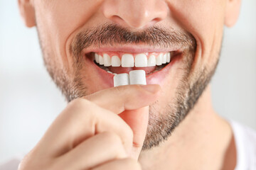 Man putting chewing gums into mouth on light background, closeup