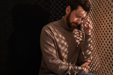 Upset man listening to priest during confession in booth, space for text