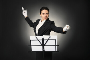 Professional conductor with baton and note stand on black background