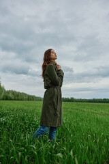 Fototapeta premium a beautiful woman in a dark coat stands in a green field in the spring in rainy weather