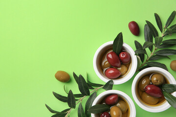 Bowls with different ripe olives and leaves on light green background, flat lay. Space for text