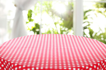 Red and white checkered tablecloth on table near window. Space for text