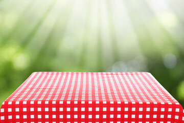 Red and white checkered tablecloth on table against green blurred background. Space for text