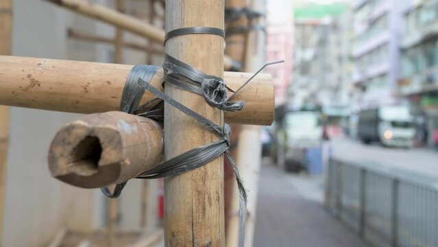Bamboo stick poles are assembled as part of a construction building scaffolding while pedestrians walk past it.