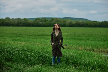 Naklejka na ściany i meble a woman stands in the middle of a green field in warm clothes. Rainy weather, walk in the forest