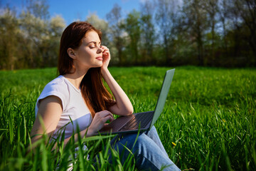 Young Caucasian woman using Laptop on nature, sitting in the grass in the park.