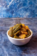 Lady Finger or Okra and Potato Curry or Gravy in White Bowl Isolated on Blue Background in Vertical Orientation
