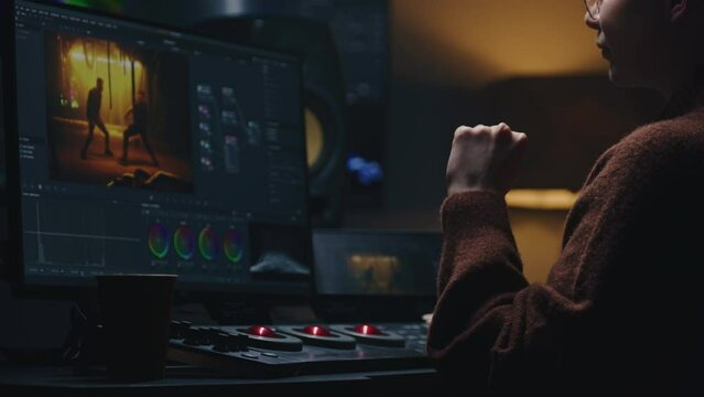 Female video maker works in studio on computer, uses color grading control panel. The colorist edits video, makes color correction for movie. Program interface with film footage, RGB wheels and levels