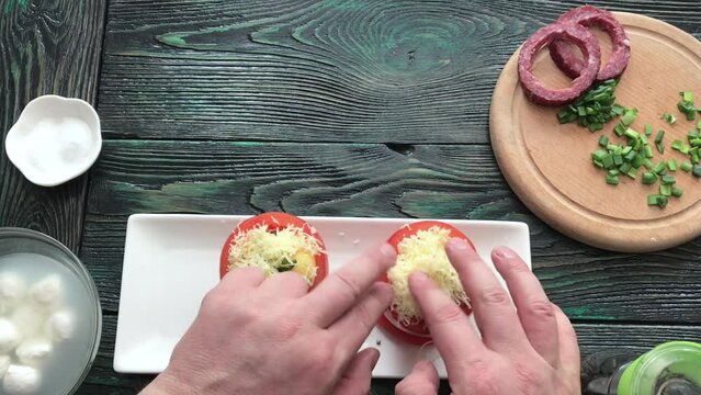 A man adds grated cheese to stuffed tomatoes. For baking in the oven. Step by step cooking. Taken from above.