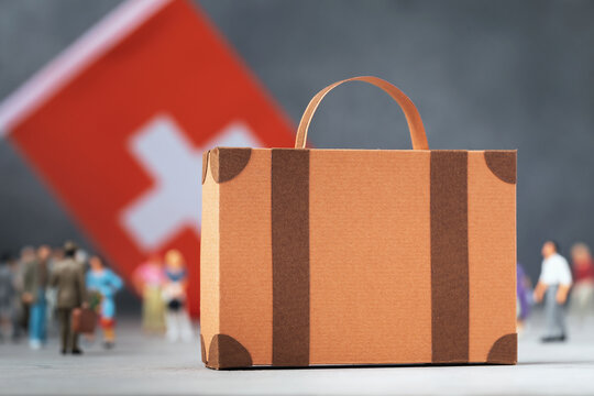 Cardboard suitcase, plastic toy people and a flag on an abstract background, a concept on the theme of moving or migration in Switzerland