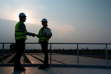 A team of electrical engineers inspecting solar panels in a hundred acres of grass on the rooftop of energy storage station, in the evening after completing the daily work tasks with the setting sun