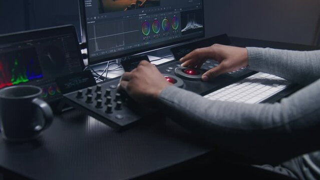Hands close up of African American video editor working by color grading control panel in studio with modern design. Colorist makes colour correction for movie post production. Professional equipment.