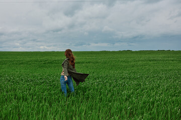 a woman in a dark coat walks through a field with tall grass in windy, rainy weather