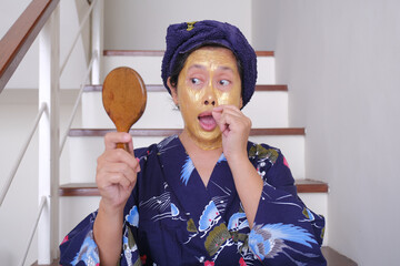 A woman looks at the mirror as she peels off her beauty mask; funny, silly expression. - obrazy, fototapety, plakaty