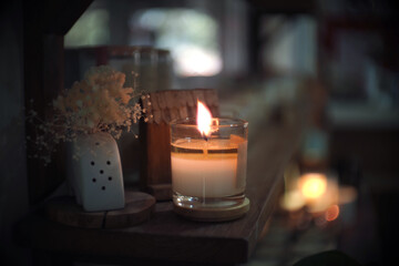 There was a vase of dried flowers on a wooden table next to an aroma candle