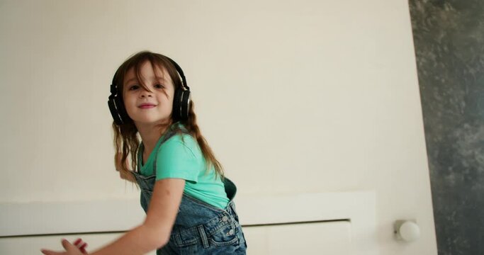 Happy little girl dancing while listening to music on smartphone with headphones in living room