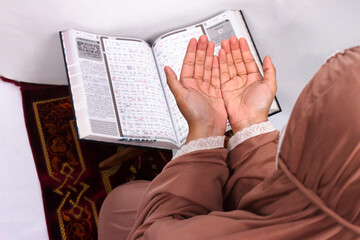 Islamic moslem woman praying Koran or Quran on praying carpet sajadah wearing traditional dress