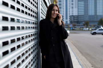 young european woman model chatting on the phone against the wall of the building