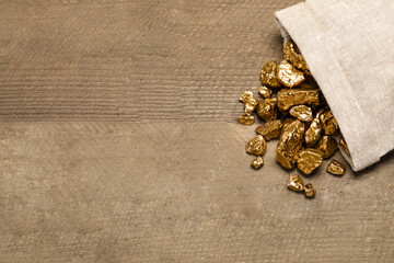 Overturned sack of gold nuggets on wooden table, flat lay. Space for text