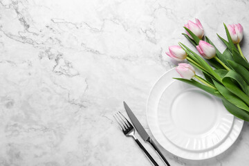 Stylish table setting with cutlery and tulips on white marble background, flat lay. Space for text