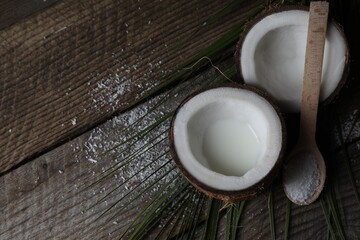 Coconut milk, flakes, nuts and palm leaf on wooden table, above view. Space for text