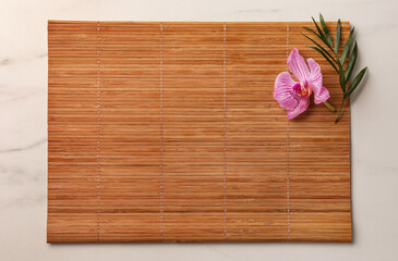 Bamboo mat, green leaf and orchid flower on white marble table, top view. Space for text