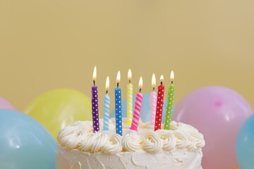 Delicious cake with burning candles and festive decor on yellow background, closeup
