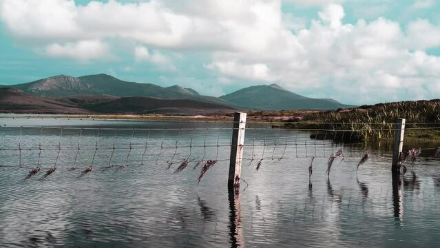 Time lapse of the clouds rolling past by a loch and a submerged fence line. A mountain range is visible in the distance. Filmed on the Isle of Uist, part of the Outer Hebrides of Scotland.