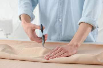 Obraz na płótnie Canvas Dressmaker cutting fabric with scissors at table in atelier, closeup