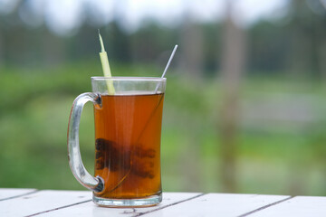 A glass of lemongrass-ginger tea on a wooden table; blurred background.