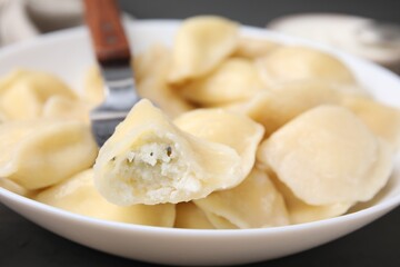 Fototapeta na wymiar Delicious dumpling (varenyk) with cottage cheese on fork over bowl, closeup