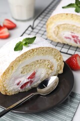 Slice of delicious sponge cake roll with strawberries and cream served on white table, closeup