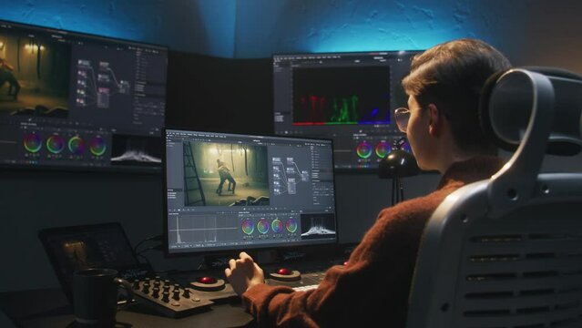 The editor works in studio on computer, uses color grading control panel, edits video, makes color correction for movie. Big screens showing program interface with film footage, RGB graphic and levels