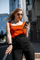 Portrait of confident woman in elegant casual clothes and using a smartphone on a city street