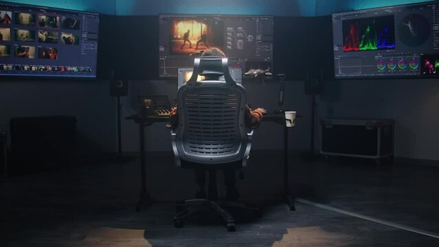 The video maker works in studio on computer, edits video, makes color grading for film post production. Big screens showing color editing program interface with movie footage, RGB graphic and levels.
