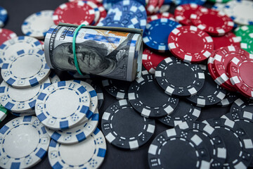 colored poker chips scattered with a roll of US dollars isolated on a black background.
