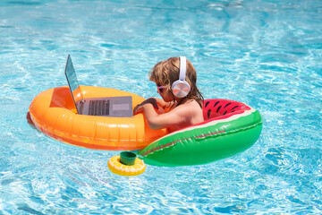 Freelance work, distance online work, e-learning. Summer business. Kid remote working on laptop in pool. Little business man working online on laptop in summer swimming pool water.