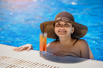 woman with a hat in the swimming pool drinking a cocktail..