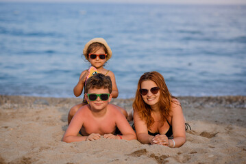 Portrait of a young family lying on the sand near a sea. Woman, girl and boy lying on the beach.