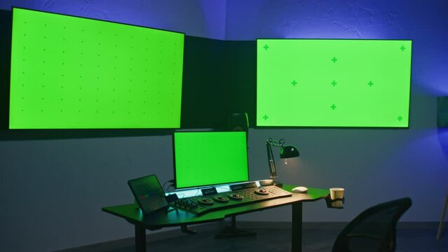 Studio with modern equipment for video or film color grading. Computer, digital tablet and big screens showing program interface, video footage. Color correction control panel. Green screen, chromakey