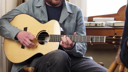 Sliding shot of a musician's fingers as he plays the acoustic guitar. A singer sings in the foreground. Filmed near Stornoway on the Isle of Lewis, part of the Outer Hebrides of Scotland.