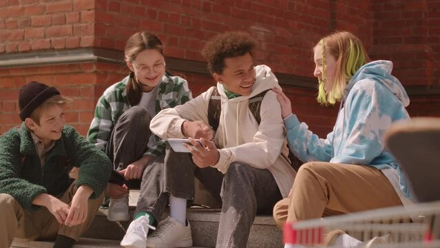 Slowmo of multiracial company of zoomers with gadgets hanging out together outdoors in summer